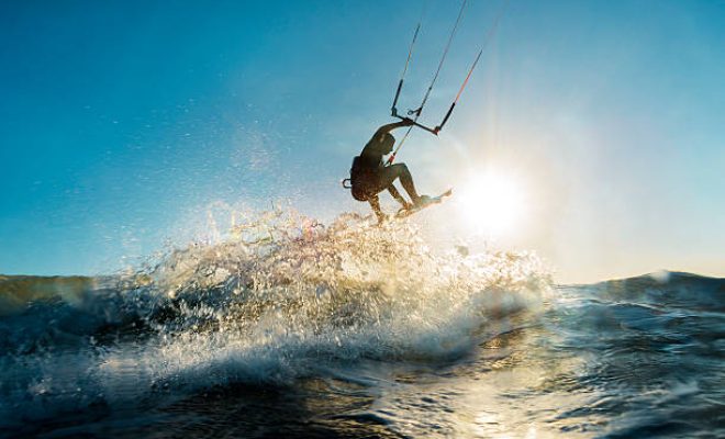 A surfer doing an amazing jump and splashing water in front of the sunset at the sea